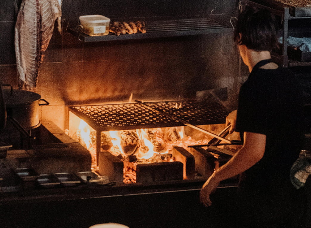 Thin-sliced meat grilling over charcoal with open flames and smoke on a restaurant BBQ grate