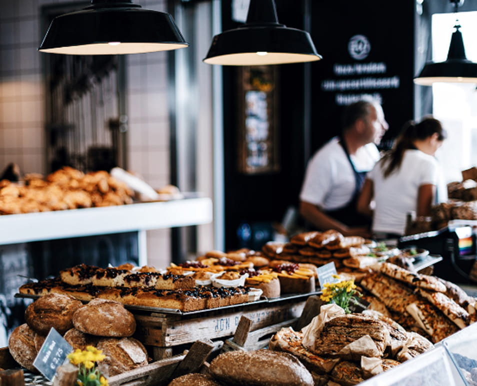 Artisan bakery counter piled with fresh loaves, baguettes, and pastries under pendant lights with staff serving guests