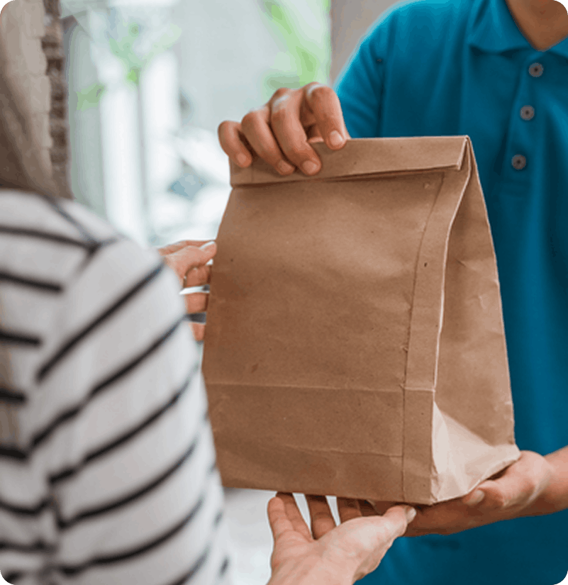 A restaurant staff handing a takeout food bag to a customer for direct online order pickup