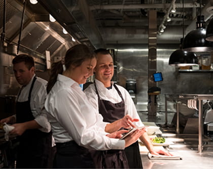 Kitchen team collaborating over a tablet in a stainless-steel restaurant kitchen