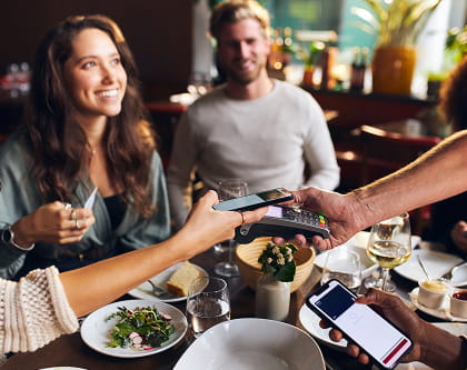 Guests at a restaurant table completing a contactless mobile payment on a handheld POS terminal